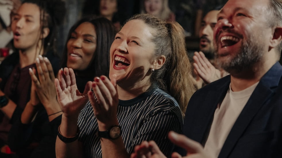 Audience laughing and applauding while watching comedy stage show in theater